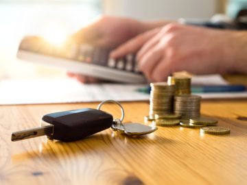 Car keys and money on table with man using calculator. Buyer counting savings an ...